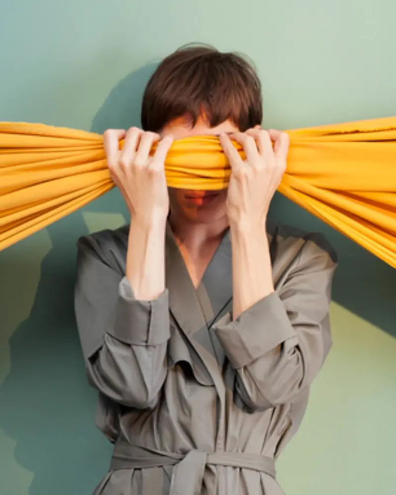 A person holding up yellow fabric over her eyes